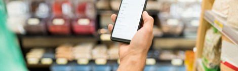 Hombre consultando la lista de la compra en su móvil en el pasillo de un supermercado