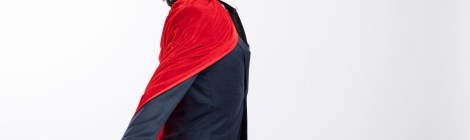 Un hombre con gafas y traje, con una capa roja de superhéroe, mira hacia arriba